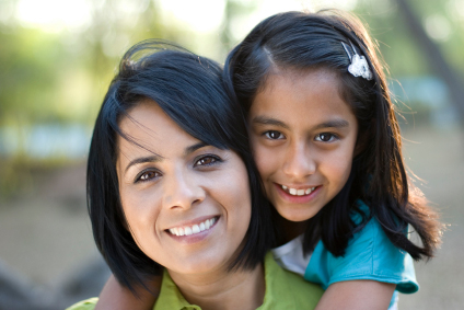 Up close picture of a young mother smiling with her daughter on her back.